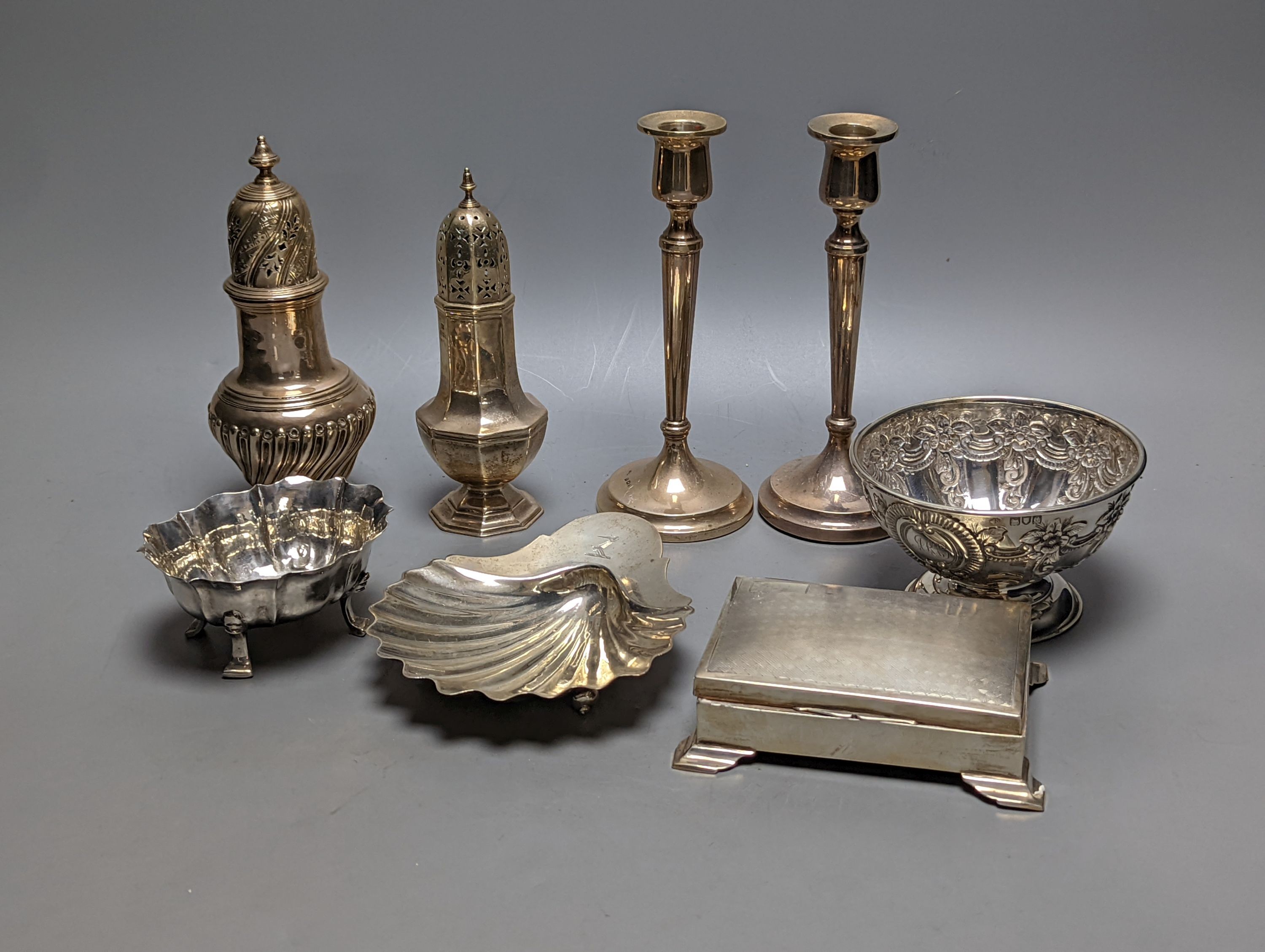 A mixed collection of silver to include a George III silver butter shell, London, 1799, a small cigarette box, two casters, a pair of slender candlesticks (loaded) and two small bowls including white metal